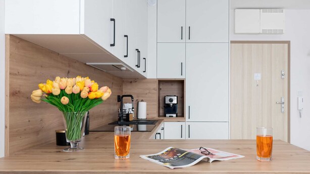 Una cocina moderna con armarios blancos, encimera de madera, una cafetera y un jarrón con tulipanes amarillos.