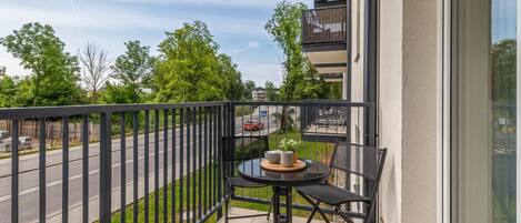 A balcony with a table and chairs, a railing, and a view of a road and greenery.