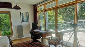 A room with a bed, desk, chair, and large windows. - Maison Moderne en Bois vue mer (Carantec)
