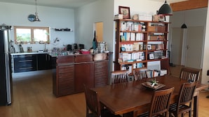 A modern kitchen with a dining area, wooden cabinets, and a bookshelf filled with books. - Maison Moderne en Bois vue mer (Carantec)