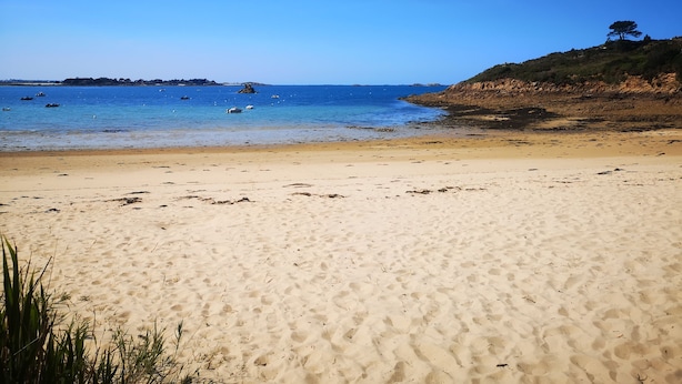 A sandy beach with clear blue water, boats, and a distant rocky coastline. - Maison Moderne en Bois vue mer (Carantec)