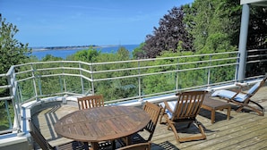 A wooden deck with a table and chairs, overlooking a body of water. - Maison Moderne en Bois vue mer (Carantec)