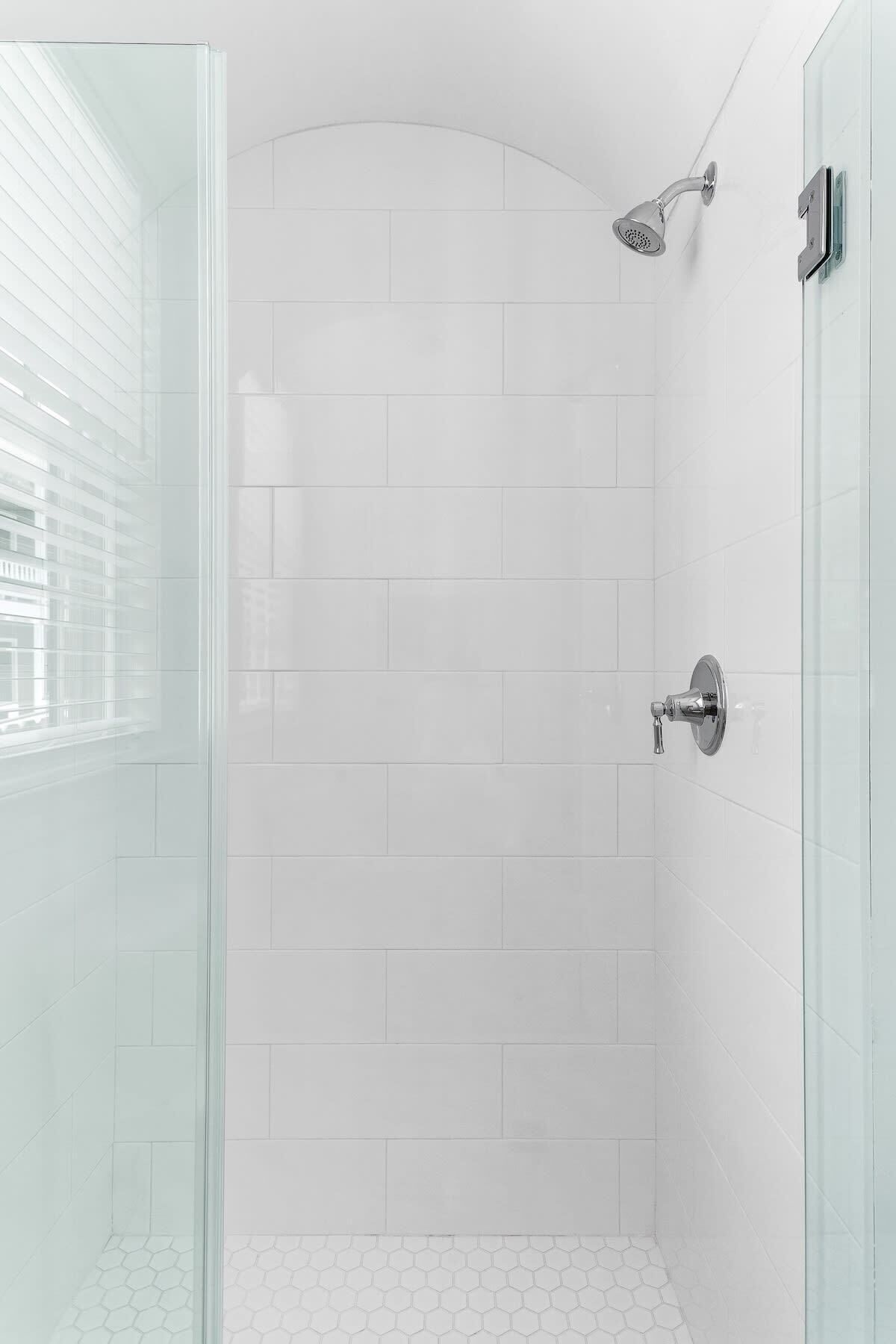 A modern shower with a glass door, white tiled walls, and a hexagonal tile floor.