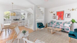 Una sala moderna con sofá, mesa de centro y sillas. Se ve una escalera que lleva a una zona de cocina.