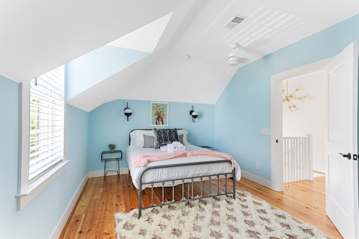 A bedroom with a sloped ceiling, a bed, a small table, and a window with blinds.
