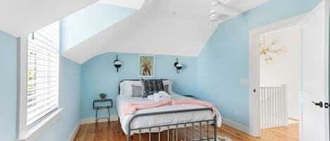 A bedroom with a sloped ceiling, a bed, a small table, and a window with blinds.