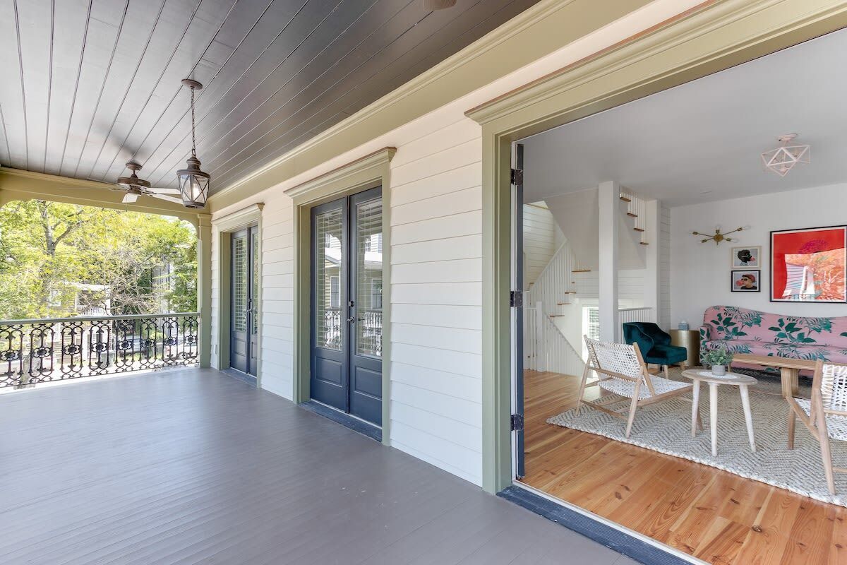 A covered porch with a ceiling fan, a wooden floor, and a view of a living room with a sofa and chairs.