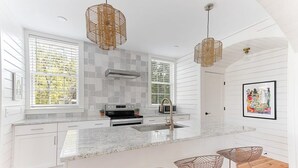 Una cocina moderna con armarios blancos, encimera de granito y una isla central con taburetes de bar.
