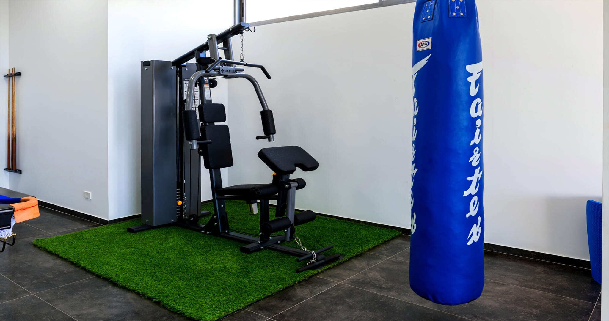 Une salle de sport équipée d’une machine de musculation, d’un banc et d’un sac de frappe bleu.