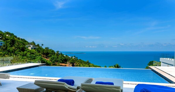 A pool with lounge chairs and a view of the ocean.