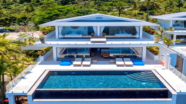 Une maison moderne à deux étages, avec une grande piscine rectangulaire située à l’avant.