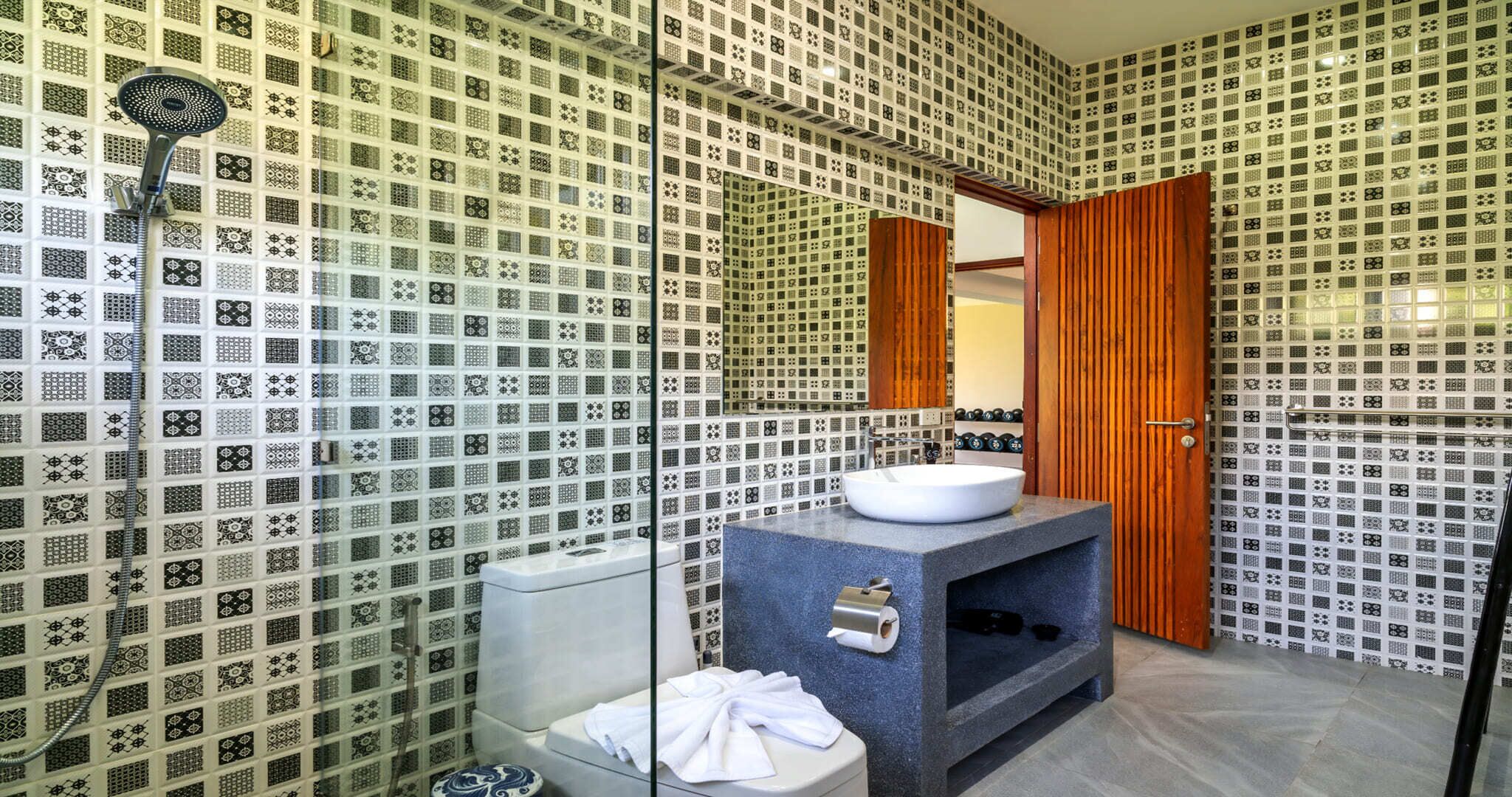 A bathroom with patterned tiles, a sink, a mirror, and a shower.
