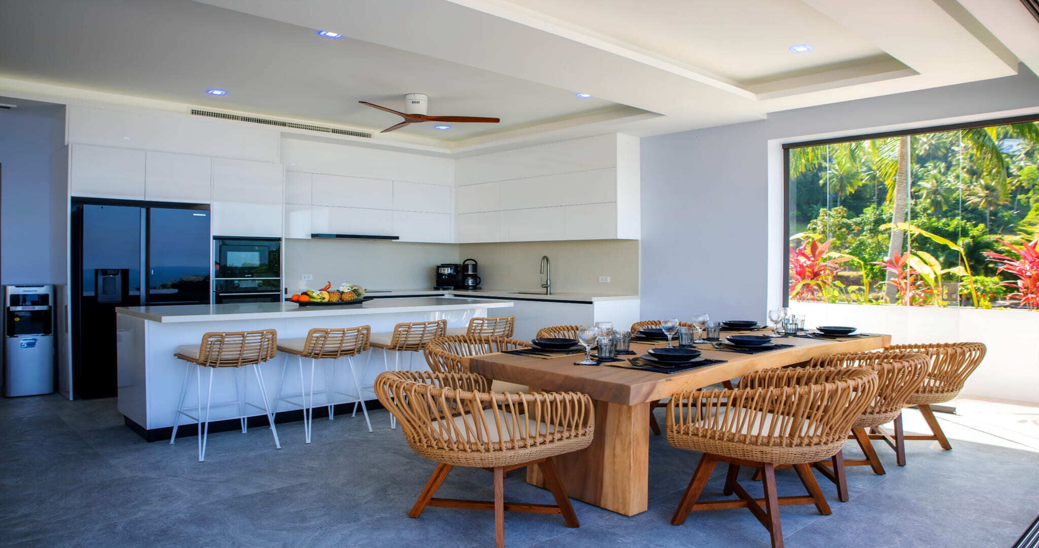 A modern kitchen with white cabinetry, a central island, and a dining area with wicker chairs.