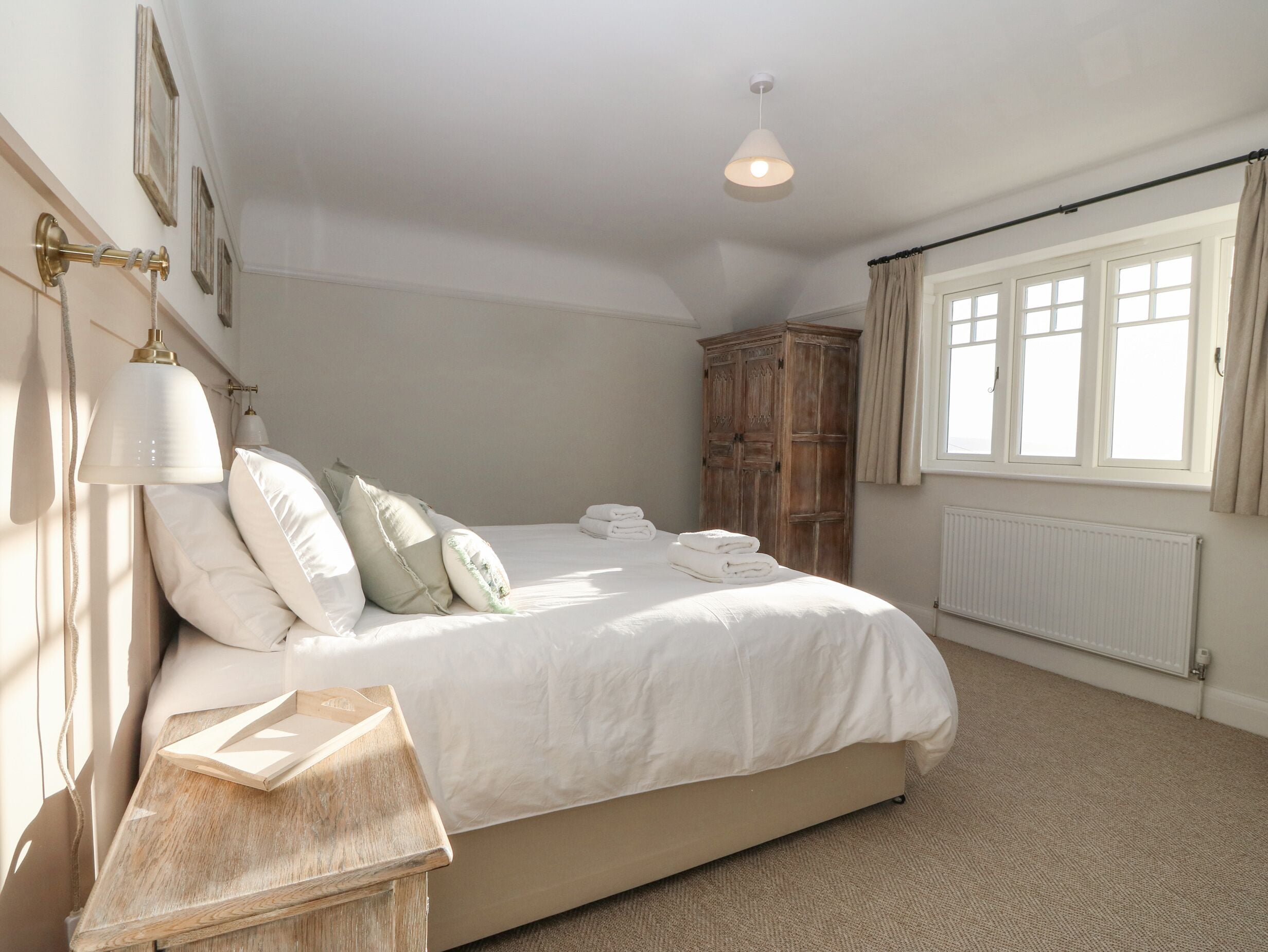 A bedroom with a bed, bedside lamps, a wooden wardrobe, and a window with curtains.