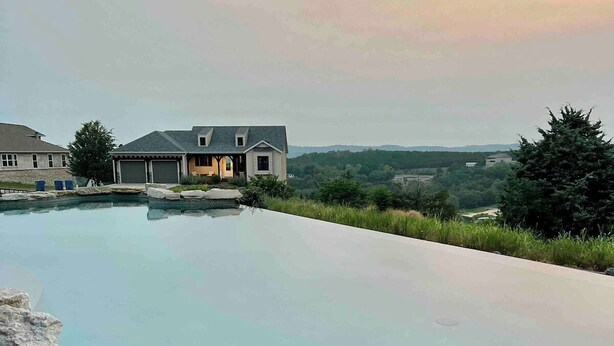 Una piscina con borde de piedra, una casa al fondo y vistas del paisaje.