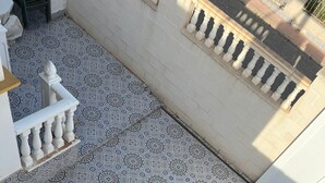 Un patio con baldosas formando un diseño geométrico, una barandilla blanca y una pared con una ventana.