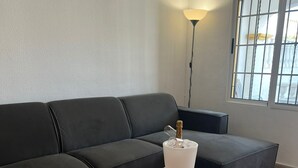 Una sala de estar moderna con un sofá gris oscuro, una mesa de centro blanca con una botella de champán y una lámpara de pie.