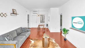 A modern living room with a sofa, a coffee table, and a dining area with a table and chairs. - Garden Suites-Hosted by Sweetstay (Miami Beach)