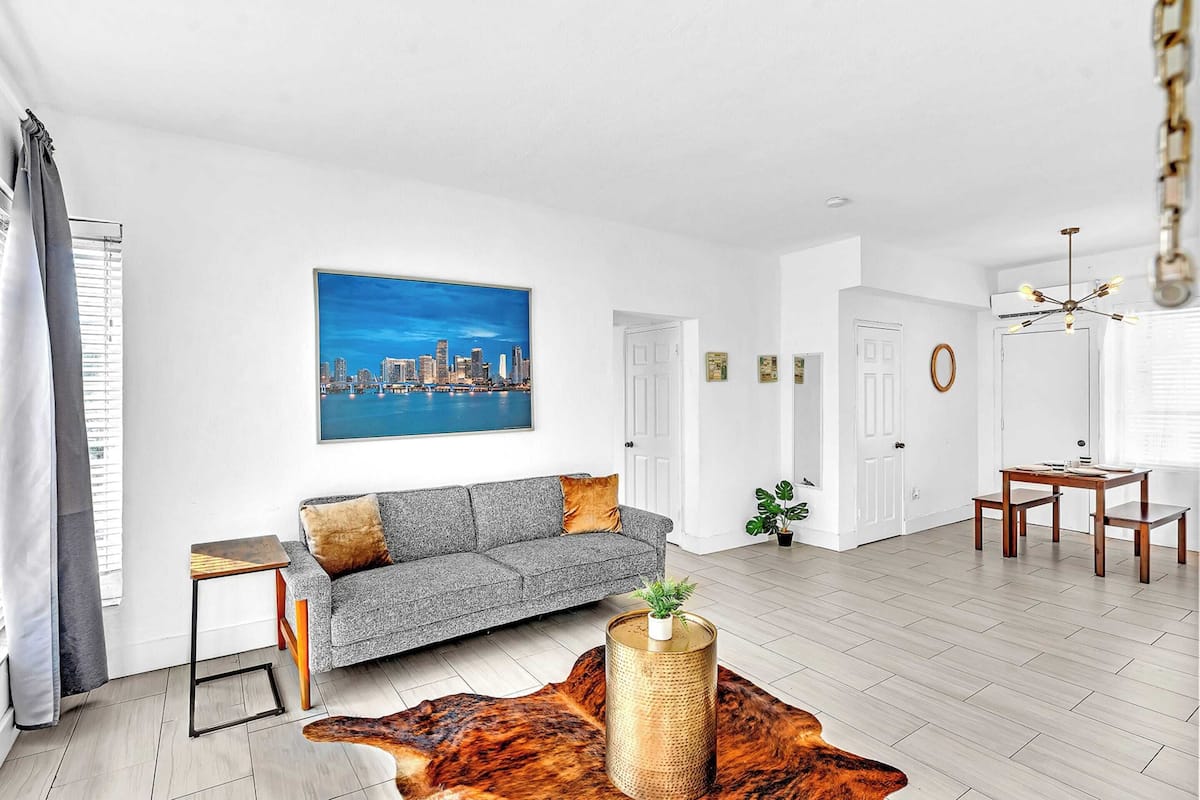 A modern living room with a grey sofa, a cityscape painting, a wooden coffee table, and a leather rug.
