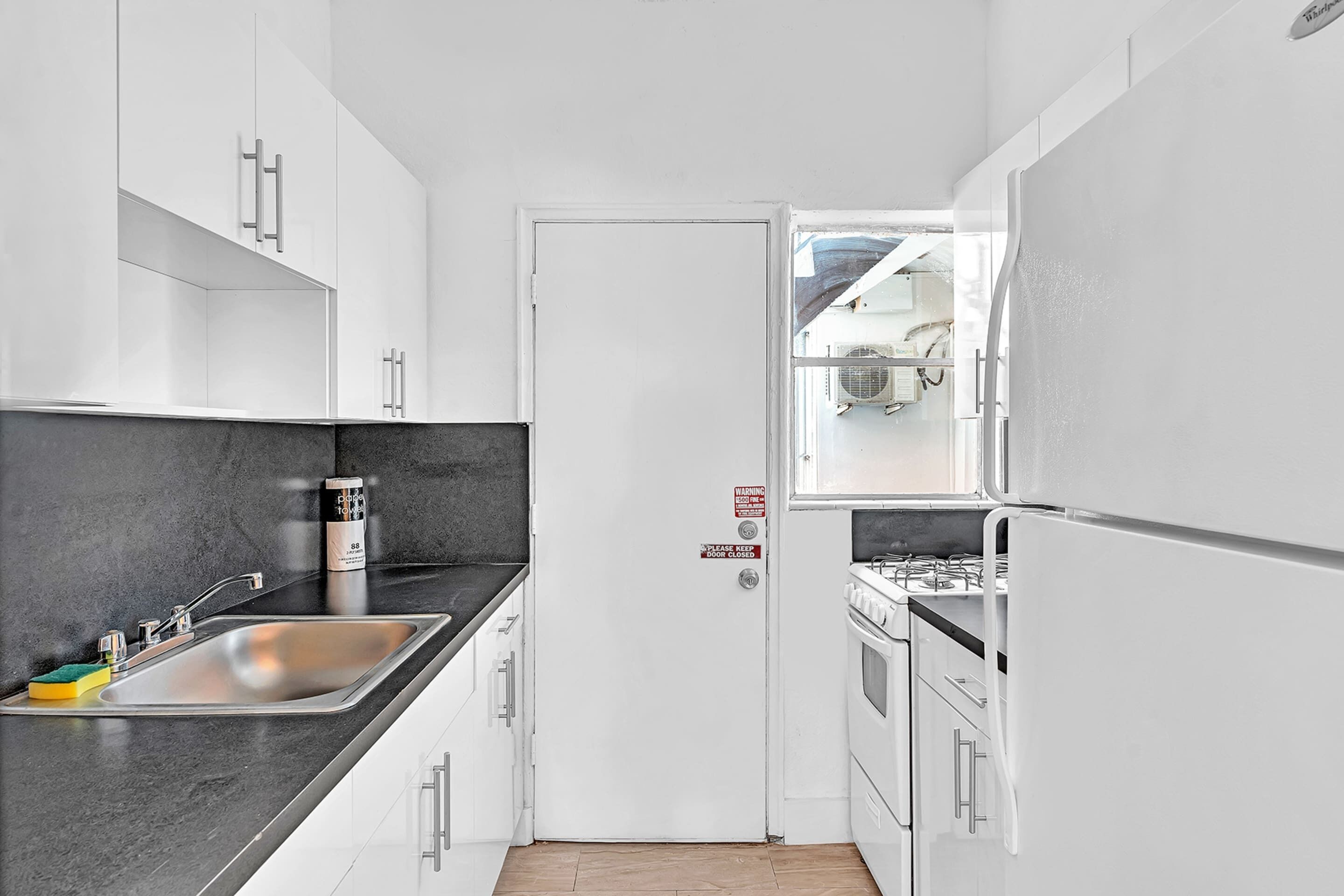 A compact kitchen with white cabinets, a black countertop, a stainless steel sink, and a stove.