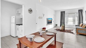 A modern kitchen with white cabinets, a refrigerator, and a dining table set with plates and cups. - Garden Suites-Hosted by Sweetstay (Miami Beach)