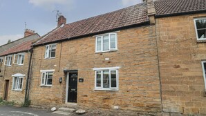 A stone cottage with a tiled roof, a black door, and white-framed windows. - Holly Cottage (Yeovil)