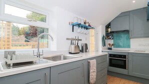 A modern kitchen with grey cabinets, a stainless steel sink, and a built-in oven. - Holly Cottage (Yeovil)