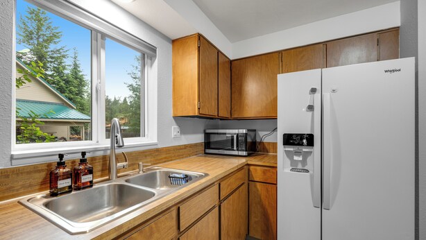 A kitchen with wooden cabinets, a stainless steel sink, a microwave, and a white refrigerator. - Baycolt McCall - Pet friendly - Near downtown and golf course - Game room - Fenced yard (McCall)