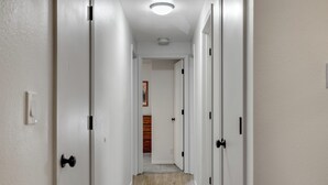 A narrow hallway with white walls and wooden flooring, leading to a room with a wooden door and a framed picture on the wall. - Baycolt McCall - Pet friendly - Near downtown and golf course - Game room - Fenced yard (McCall)