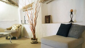 Una sala de estar con un sofá color beige, una mesita de centro, un sillón con cojines estampados, un jarrón decorativo con ramas y un cuadro en la pared.