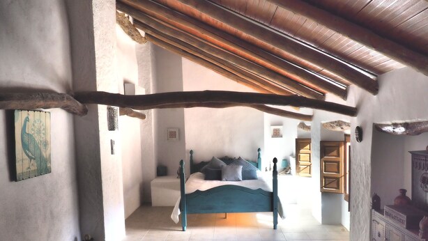 Un dormitorio con cama, alfombra estampada y viga de madera en el techo.