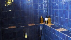 Un baño con paredes de azulejos azules, un cabezal de ducha y dos accesorios dorados en la pared.
