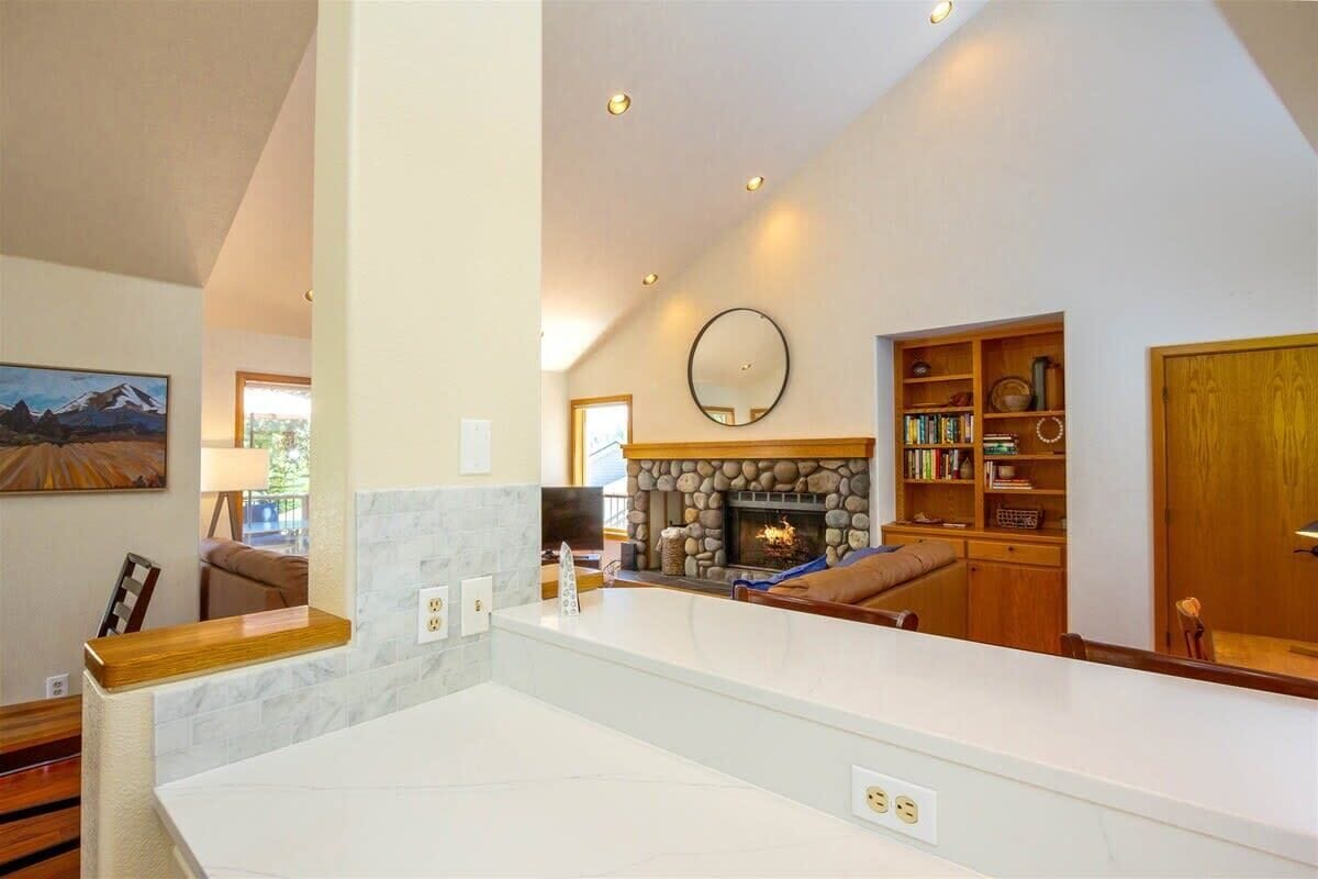 A modern living room with a stone fireplace, a wooden bookshelf, and a large mirror on the wall.