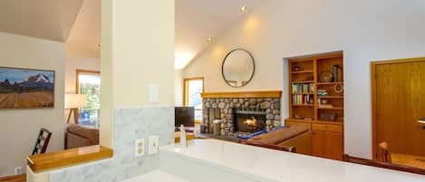 A modern living room with a stone fireplace, a wooden bookshelf, and a large mirror on the wall.