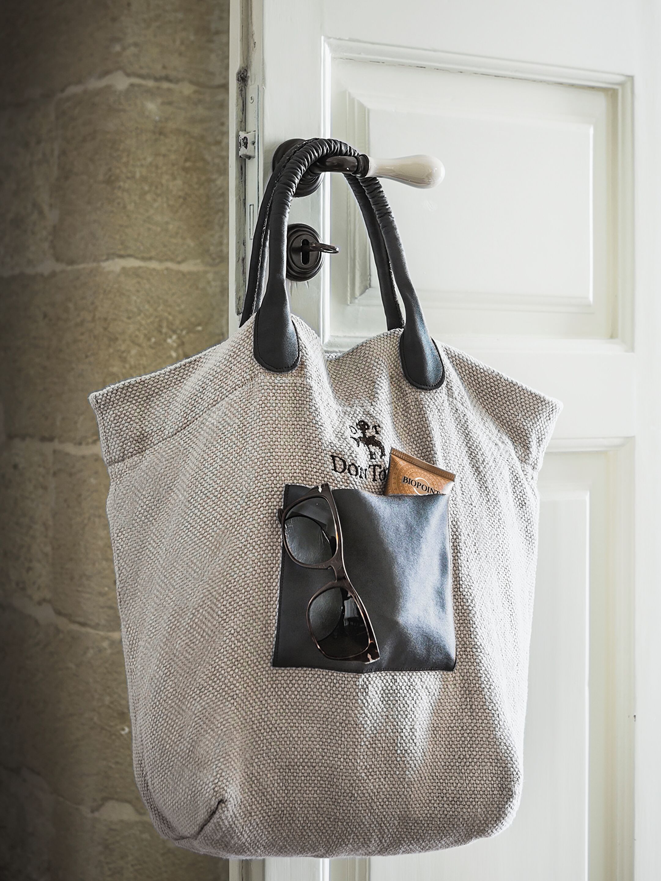 Un grand sac fourre-tout en tissu, suspendu à une poignée de porte.
