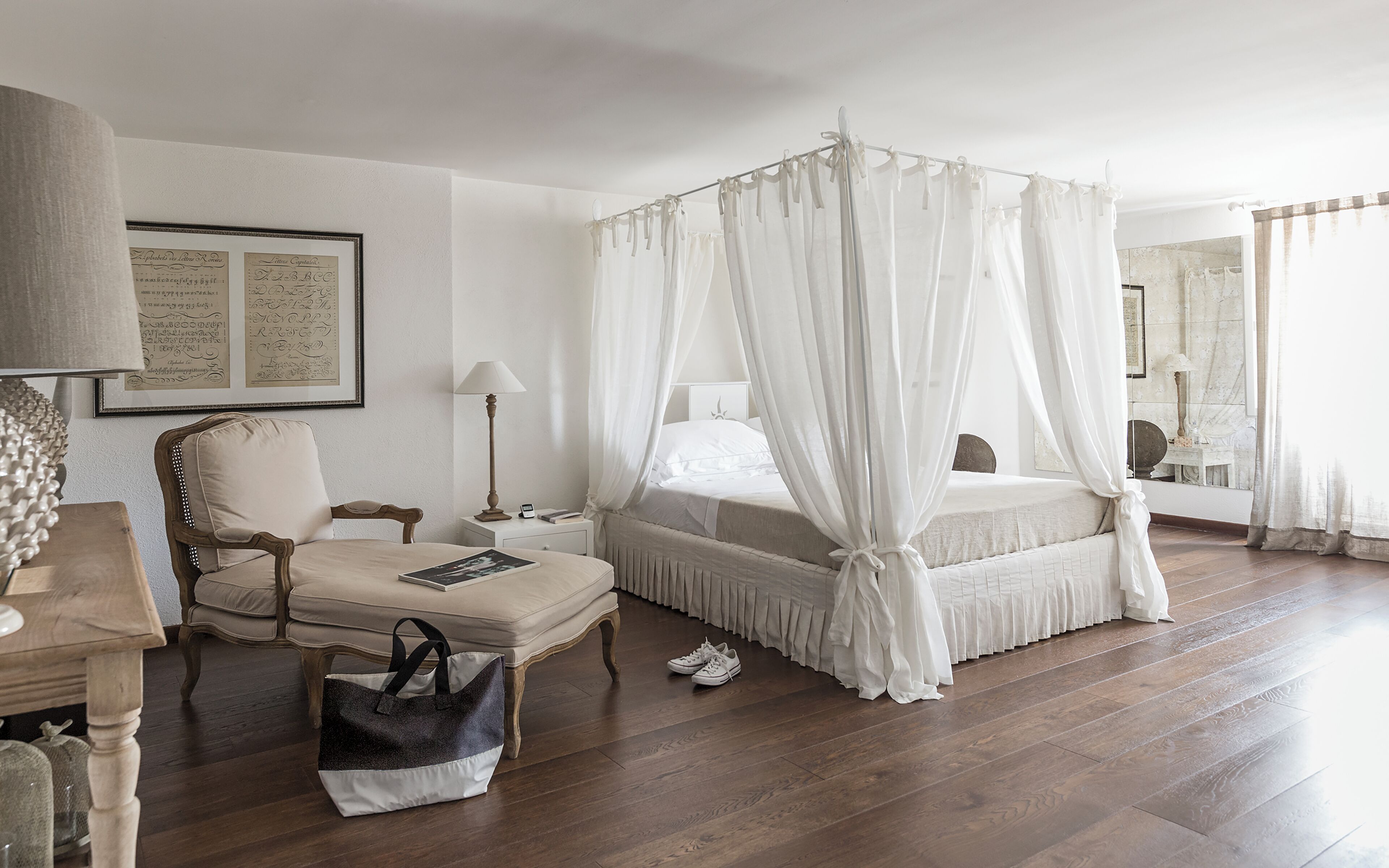 A bedroom with a four-poster bed, a chair, a bedside table, and a nightstand.