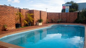 A swimming pool with a brick wall, potted plants, and a sign for a motel in the background. - Yambil Inn Motel (Griffith)