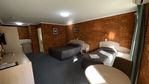 A compact room with two beds, a small table, a kitchenette, and a brick wall.