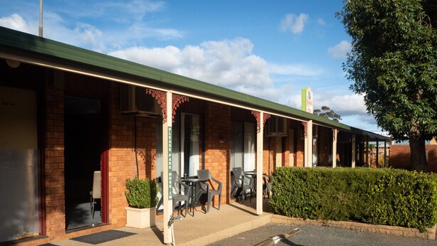 A brick building with a green roof, outdoor seating, and a hedge. - Yambil Inn Motel (Griffith)