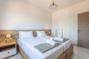 A double bed with white linens, a wooden nightstand with a lamp, and a bedside table with a towel and a robe. - Villa Sandi with Private Pool (Heraklion)