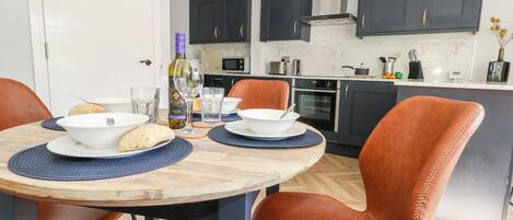 A modern kitchen with dark cabinets, a central island, and a dining area with a round table and leather chairs.