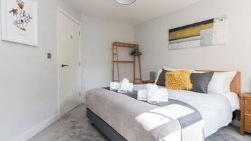 A neatly arranged bedroom with a bed, a ladder, and a painting on the wall.