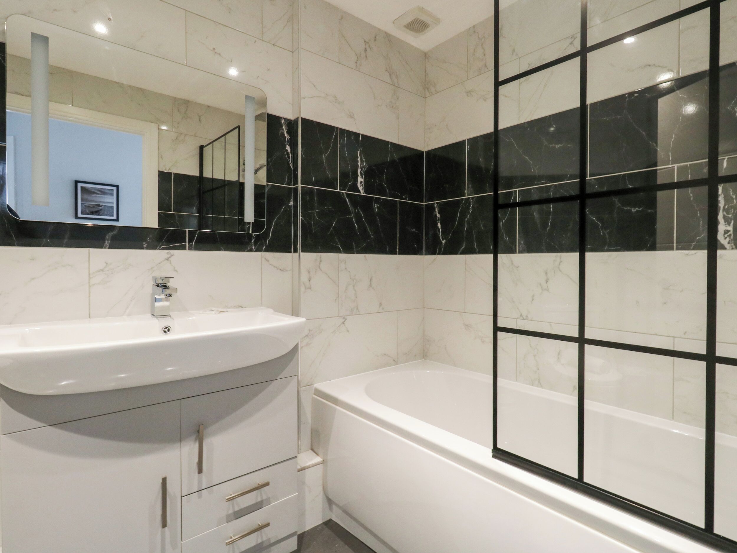 A modern bathroom with a white sink, a bathtub, and black marble tiles.