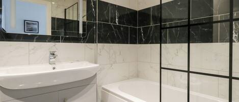 A modern bathroom with a white sink, a bathtub, and black marble tiles.