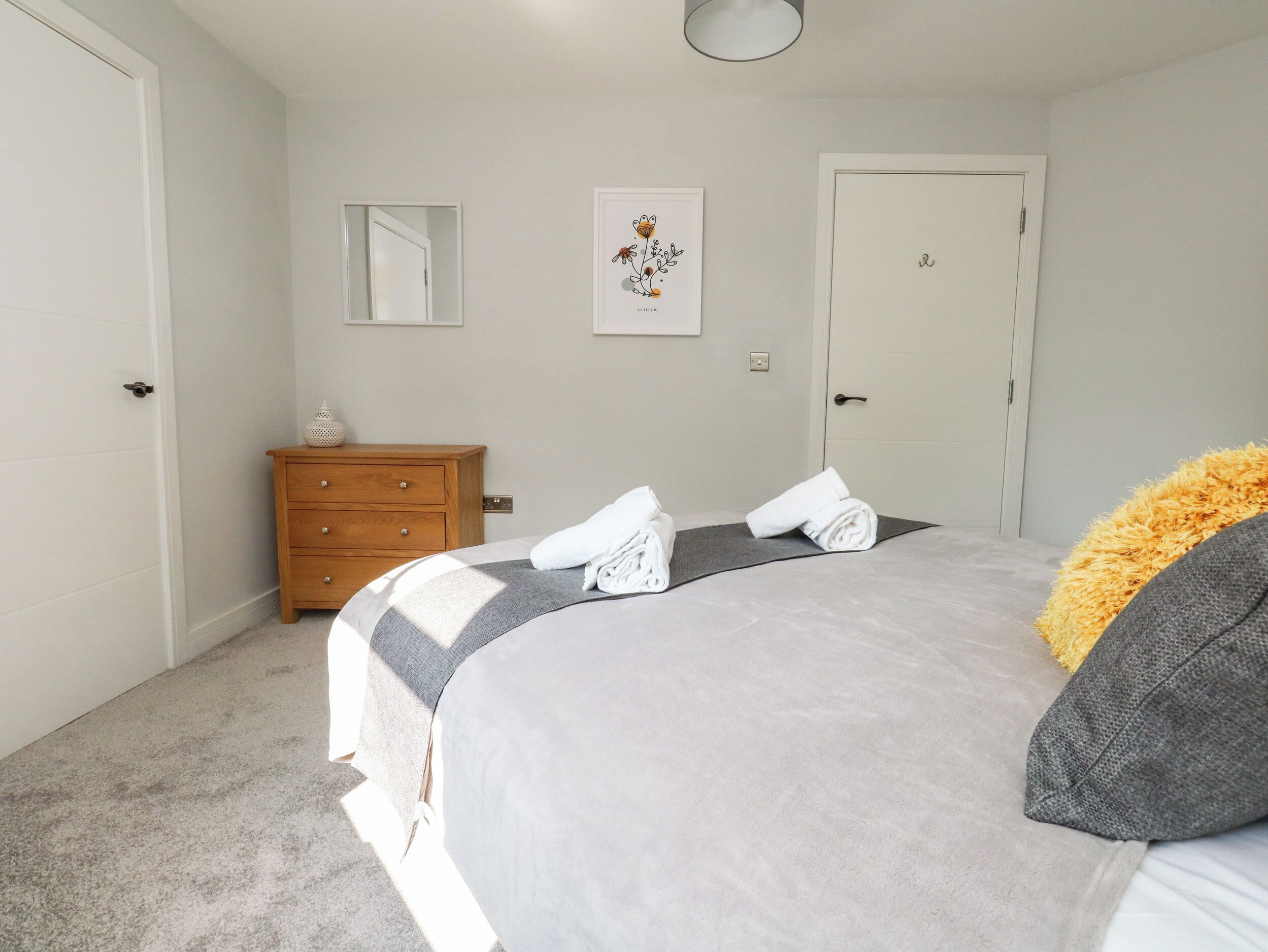 Ein Schlafzimmer mit Bett, Kommode, Spiegel und Tür.