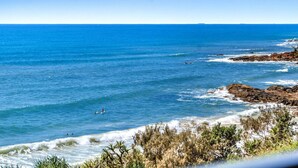 A coastal view with clear blue waters, rocky shoreline, and vegetation. - Absolute Beachfront Luxury Apartment (Coolum Beach)
