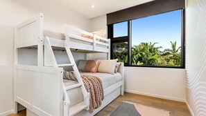 Una cama litera con escalera, un sofá y una ventana con vista a follaje.