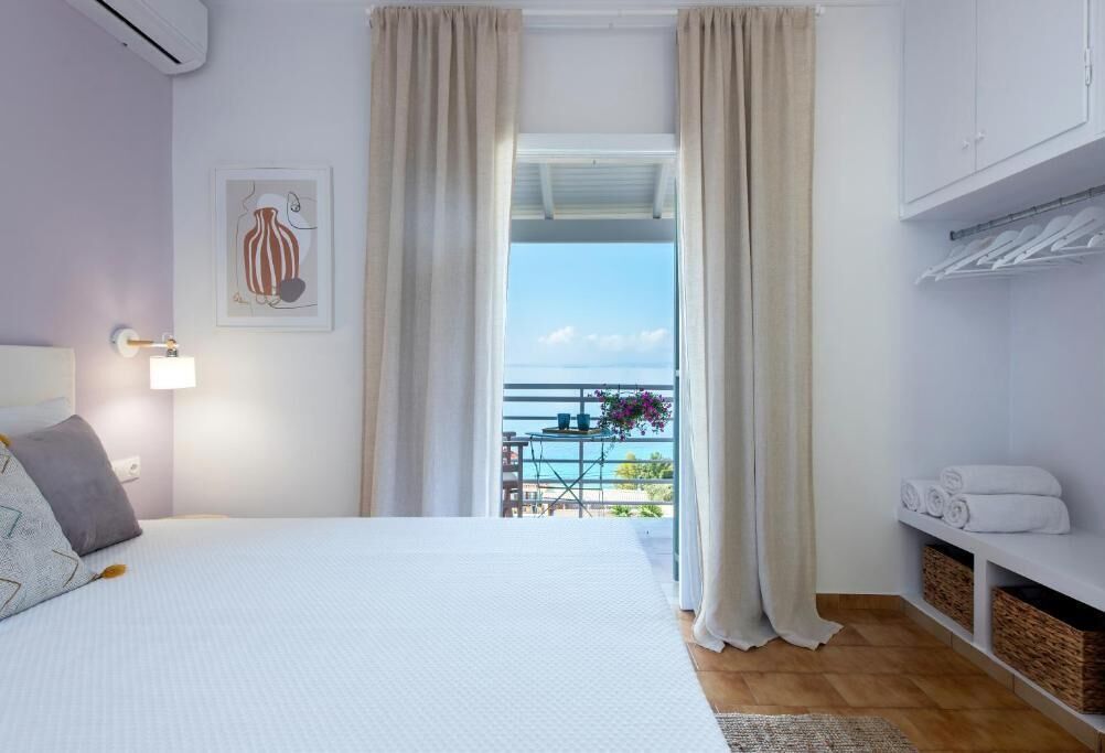 Une chambre avec un lit, une table de chevet, une lampe fixée au mur, un tableau encadré, un balcon avec vue et une étagère avec des serviettes.