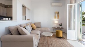 A modern living room with a beige sofa, a small round table, a yellow ottoman, and a view of the outdoors through a glass door. - Reana Elegant Apartments by Konnect, Barbati (Corfu)
