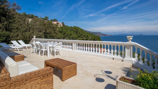 Une terrasse dotée de mobilier d’extérieur blanc, d’un canapé en osier et offrant une vue sur la mer et les collines.